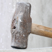 Image: A well-worn sledgehammer, resting on a ledge.