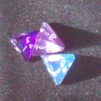 Three four-sided dice, in purple and blue, sitting on a dark grey cloth tablecloth. They are lit by bright light from the left, with many internal reflections and casting triangular shadows to the right.